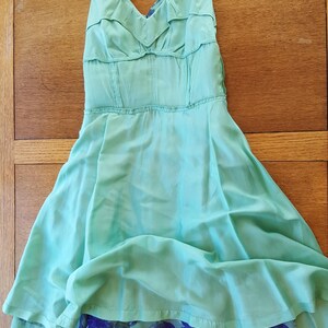 May include: A light turquoise halter dress with a flowing skirt. The dress features a ruffled bodice and a contrasting blue floral print at the hem. The dress is made of a lightweight fabric.