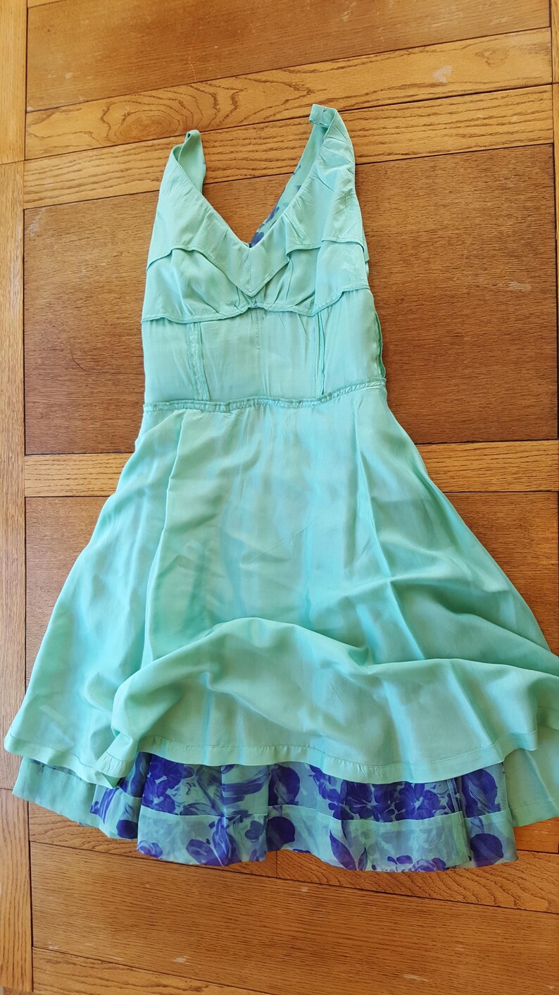 May include: A light turquoise halter dress with a flowing skirt. The dress features a ruffled bodice and a contrasting blue floral print at the hem. The dress is made of a lightweight fabric.