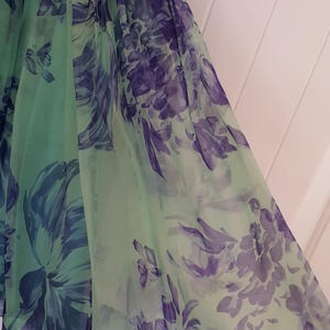 May include: A flowing, light green dress with a floral pattern in shades of purple and blue. The fabric appears to be sheer, with a layered design. The dress has a gathered bodice and a flared skirt.