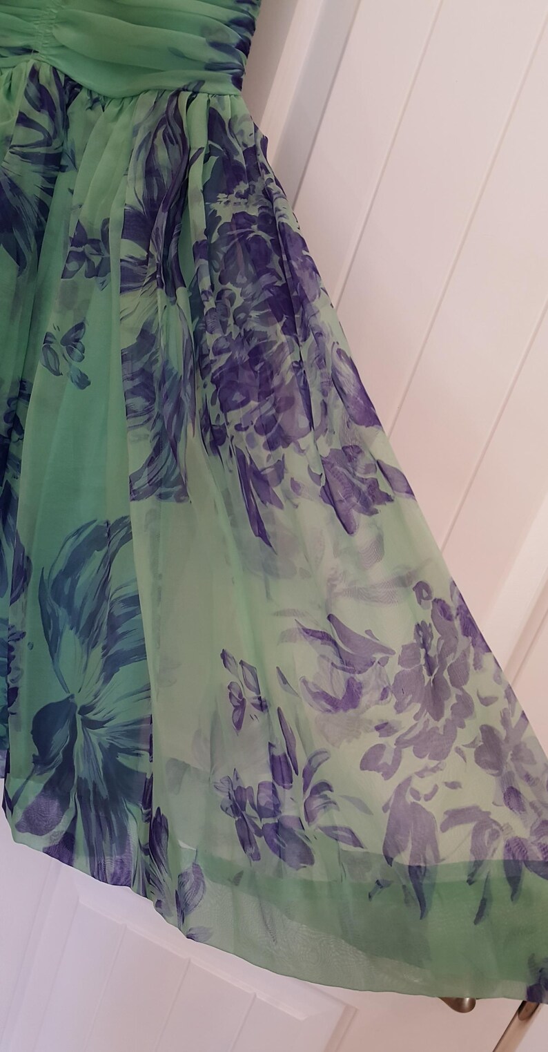 May include: A flowing, light green dress with a floral pattern in shades of purple and blue. The fabric appears to be sheer, with a layered design. The dress has a gathered bodice and a flared skirt.