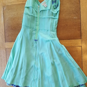 May include: A light turquoise dress with a V-neckline and a full skirt. The dress features a front zipper and a contrasting floral pattern on the lining. The dress is made of a lightweight fabric, perfect for warm weather.