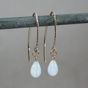 May include: A pair of gold drop earrings with white opal teardrop stones. The earrings have a textured wire design.