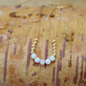 May include: A gold chain necklace with white opal beads. The necklace is on a light brown wooden surface.
