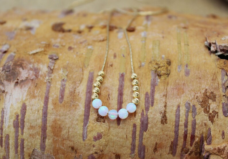 May include: A gold chain necklace with white opal beads. The necklace is on a light brown wooden surface.