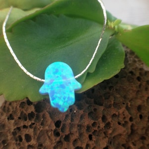 May include: A silver chain necklace with a blue opal hamsa hand pendant.