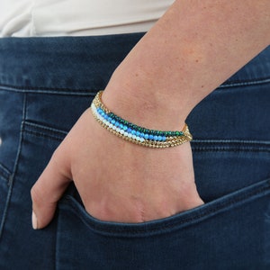 Op de afbeelding: Een stapel van vier armbanden met gouden, witte, blauwe en groene kralen.