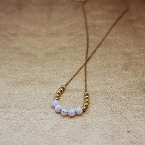 May include: A gold chain necklace with a row of iridescent white beads.