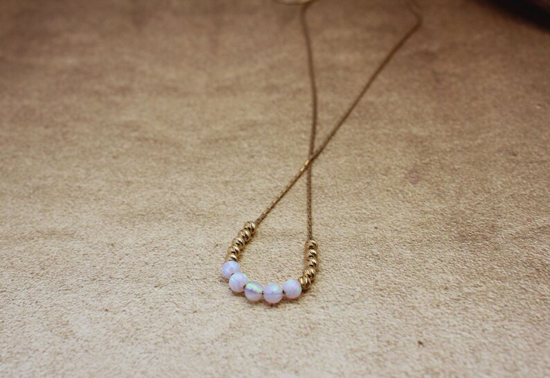 May include: A gold chain necklace with a row of iridescent white beads.