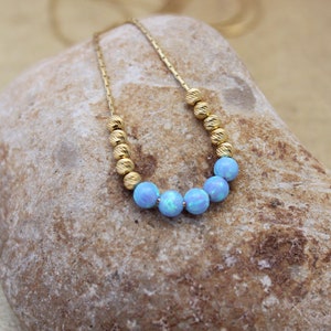 May include: A delicate gold chain necklace with a row of light blue opal beads.