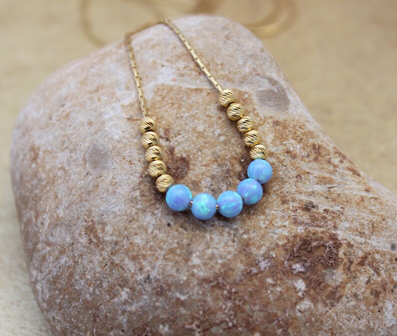 May include: A delicate gold chain necklace with a row of light blue opal beads.