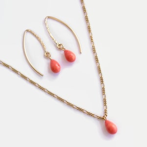 May include: A gold chain necklace and matching earrings with a teardrop-shaped coral pendant.
