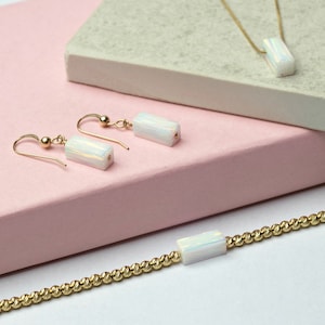 Könnte beinhalten: Ein Schmuckset mit einer goldenen Halskette, einem Armband und Ohrringen. Jedes Stück hat eine rechteckige, irisierende weiße Perle. Die Ohrringe sind im Tropfenstil gehalten, und das Armband und die Halskette haben eine goldene Kette.