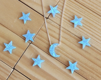 Könnte beinhalten: Eine silberne Halskette mit einem Mond-Anhänger und blauen sternförmigen Charms. Mond und Sterne haben ein schimmerndes Aussehen. Die Kette und Charms liegen auf einem Holzgrund.