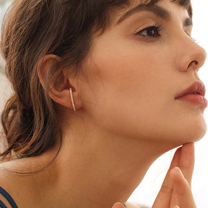 Può includere: Una donna indossa un semplice orecchino a cerchio d'oro con una fila di piccoli diamanti.