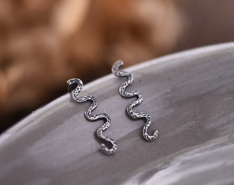 May include: A pair of silver earrings with a wavy, textured design. The earrings are small and delicate, and they would be a great addition to any jewelry collection.