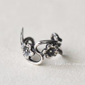 May include: Silver ear cuff with a delicate floral design. The cuff features three small flowers with intricate details.