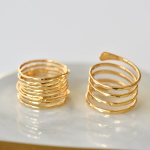 Peut inclure: Deux bagues en or, l'une est une pile de bagues fines et l'autre est une bague unique enroulée. Les deux bagues ont une texture martelée.