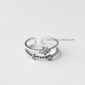 Puede incluir: Anillo de plata con un dije de estrella y un dije de corazón. El anillo es ajustable y tiene una banda de cuentas.