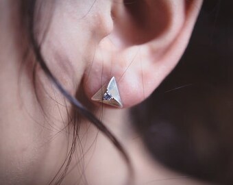 May include: A silver triangle earring with a small clear stone in the center.