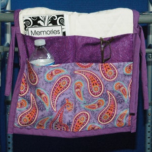 May include: A purple fabric walker bag with paisley print, featuring a clear water bottle, a book titled "Memories", and glasses in a pocket.