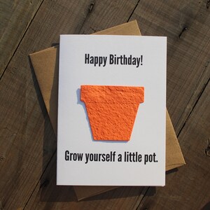 May include: A white card with the text "Happy Birthday!" and "Grow yourself a little pot."  A small orange paper pot is attached to the card.