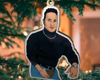 Può includere: Un ornamento natalizio in legno con un'illustrazione a cartone animato di un uomo che indossa un maglione a collo alto nero e jeans blu. L'ornamento è appeso a uno spago verde.