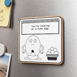 May include: A rectangular wooden magnet with a white background and a black and white cartoon egg design. The text "You're looking at a nude egg" is at the top. A basket of eggs is on the right.
