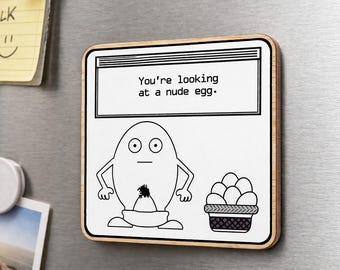 May include: A rectangular wooden magnet with a white background and a black and white cartoon egg design. The text "You're looking at a nude egg" is at the top. A basket of eggs is on the right.