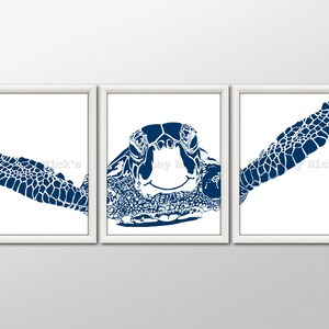 May include: A set of three blue and white silhouette prints of a sea turtle. The prints are framed in white frames and are arranged in a row on a white wall.