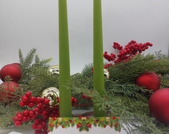 May include: Two green bayberry candles with flames burning, surrounded by red and gold Christmas decorations and greenery. The text on the card reads: "This bayberry candle comes from a friend. So on Christmas Eve burn it down to the end. When candle burned to the socked, find gold to the pocket! Merry Christmas".