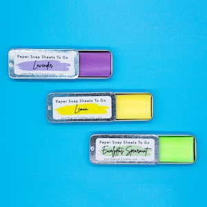 May include: Three small metal tins containing paper soap sheets. The tins are labeled with the scents Lavender, Lemon, and Eucalyptus Spearmint. Each tin has a small, colorful soap sheet inside.