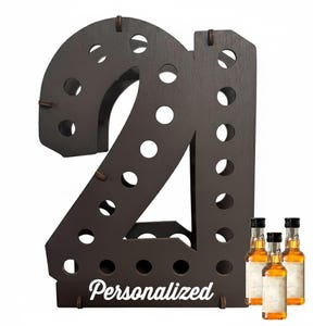 May include: A dark brown wooden display stand shaped like the number 21, featuring multiple circular cutouts for holding small bottles. The word Personalized is printed in white script at the base, accompanied by three small glass liquor bottles.