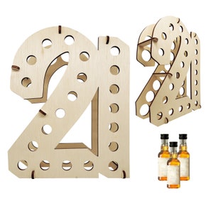 May include: A light-colored wooden display stand shaped like the number 21, featuring multiple circular cutouts designed to hold small bottles. The structure is assembled from flat wooden panels with visible slots and includes three miniature bottles.