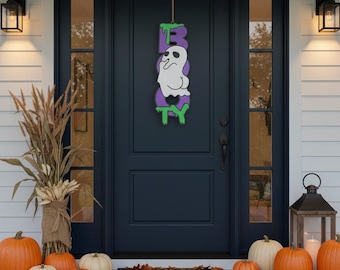 May include: A vertical hanging sign featuring the word BOOTY in purple block letters with green slime accents. A white ghost with black eyes and a mouth is positioned in the centre of the sign, replacing the letter O. The sign hangs from a brown cord.