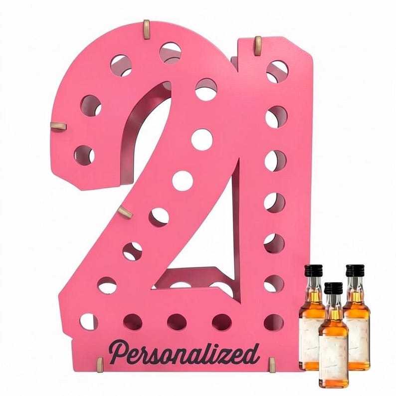 May include: A bright pink wooden display stand shaped like the number 21, featuring multiple circular cutouts for holding small bottles. The word Personalized is printed in black script at the base, accompanied by three small glass liquor bottles.