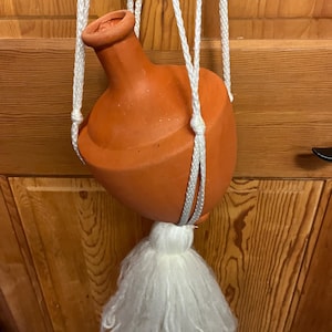May include: A terracotta hanging planter with a white tassel. The planter is suspended from a white rope.
