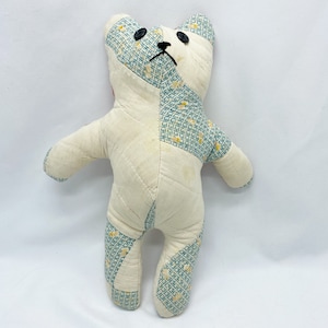 May include: A handmade patchwork teddy bear with a white body and blue and yellow patterned arms and legs. The bear has black button eyes and a black nose.