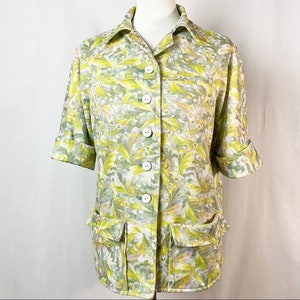 May include: A vintage button-up shirt with a green, yellow, and white swirl pattern. The shirt has a collared neckline, long sleeves, and two large pockets on the front.