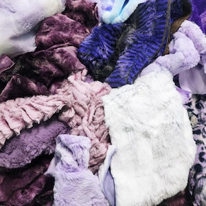 May include: A close-up shot of a pile of plush, faux fur fabrics in various shades of purple, lavender, and white. The textures vary from smooth to shaggy, with some pieces featuring animal print patterns. The fabrics appear soft and luxurious.