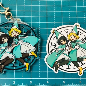 May include: Two cartoon characters wearing blue and white hats and robes, holding hands and running in a circle. The characters are on a clear acrylic keychain and a white sticker.
