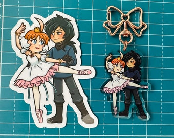 May include: A pair of illustrated characters, a girl in a pink and white ballerina costume and a boy in a blue shirt and black pants, are dancing together. The image is a printed design on a clear acrylic charm with a gold bow and chain.