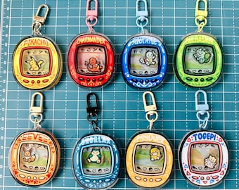 Puede incluir: Nueve llaveros digitales de mascotas coloridos con diferentes personajes de Pokémon. Los llaveros son redondos y tienen una pantalla que muestra los Pokémon. Los llaveros están unidos a cadenas plateadas.