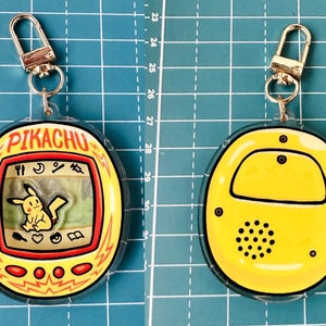 May include: A yellow and red plastic keychain shaped like a Pikachu Tamagotchi. The keychain has a silver metal clasp. The front of the keychain shows a digital screen with a cartoon Pikachu on it. The back of the keychain is yellow with a black speaker.