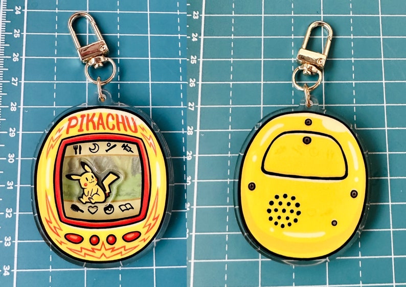 May include: A yellow and red plastic keychain shaped like a Pikachu Tamagotchi. The keychain has a silver metal clasp. The front of the keychain shows a digital screen with a cartoon Pikachu on it. The back of the keychain is yellow with a black speaker.