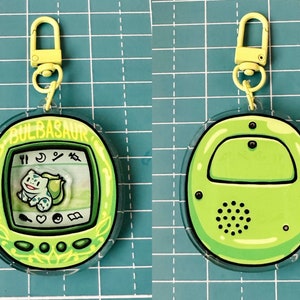 May include: A green and yellow Pokemon-themed keychain with a clear plastic casing. The front of the keychain features a digital pet screen with the text "BULBASAUR" and an image of the Pokemon character. The back of the keychain is plain green.