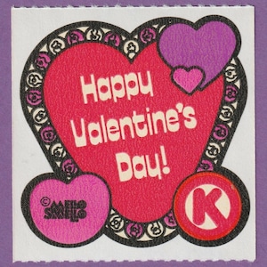 Puede incluir: Una tarjeta de San Valentín con un corazón rojo que dice "Happy Valentine's Day!" El corazón está rodeado por un borde blanco y negro con un corazón rosa y un corazón morado en la parte superior. Hay un corazón rosa con la palabra "SMILES" a la izquierda y un círculo rojo con una "K" blanca a la derecha.