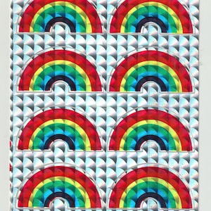 May include: A sheet of rainbow stickers with a holographic background. The stickers are arranged in rows of two, with each sticker featuring a rainbow arch.