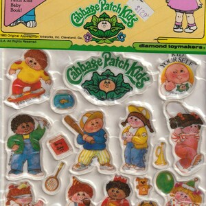 Könnte beinhalten: Ein Bogen mit Puffy-Stickern mit Cabbage Patch Kids-Charakteren. Die Aufkleber zeigen Kinder mit Spielzeug und den Texten "Sweet Dreams" und "Giggles". Die Verpackung trägt die Aufschrift "Puffy Stick-Ons".