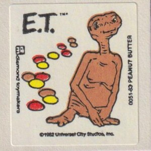 以下が含まれることがあります： 映画のキャラクターE.T.が登場するヴィンテージステッカー。茶色の宇宙人は長い首と大きな目で座っています。ステッカーには「E.T.」と「0051-83 PEANUT BUTTER」の文字が入っています。カラフルな形も存在します。