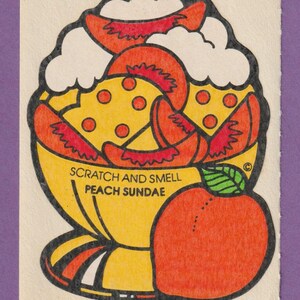 Puede incluir: Una pegatina para rascar y oler de un sundae de melocotón. El sundae está en una taza amarilla con una base a rayas rojas y blancas. Hay tres rodajas de melocotón encima del sundae, con crema batida y una cereza. Un melocotón entero está en el lado derecho de la pegatina.